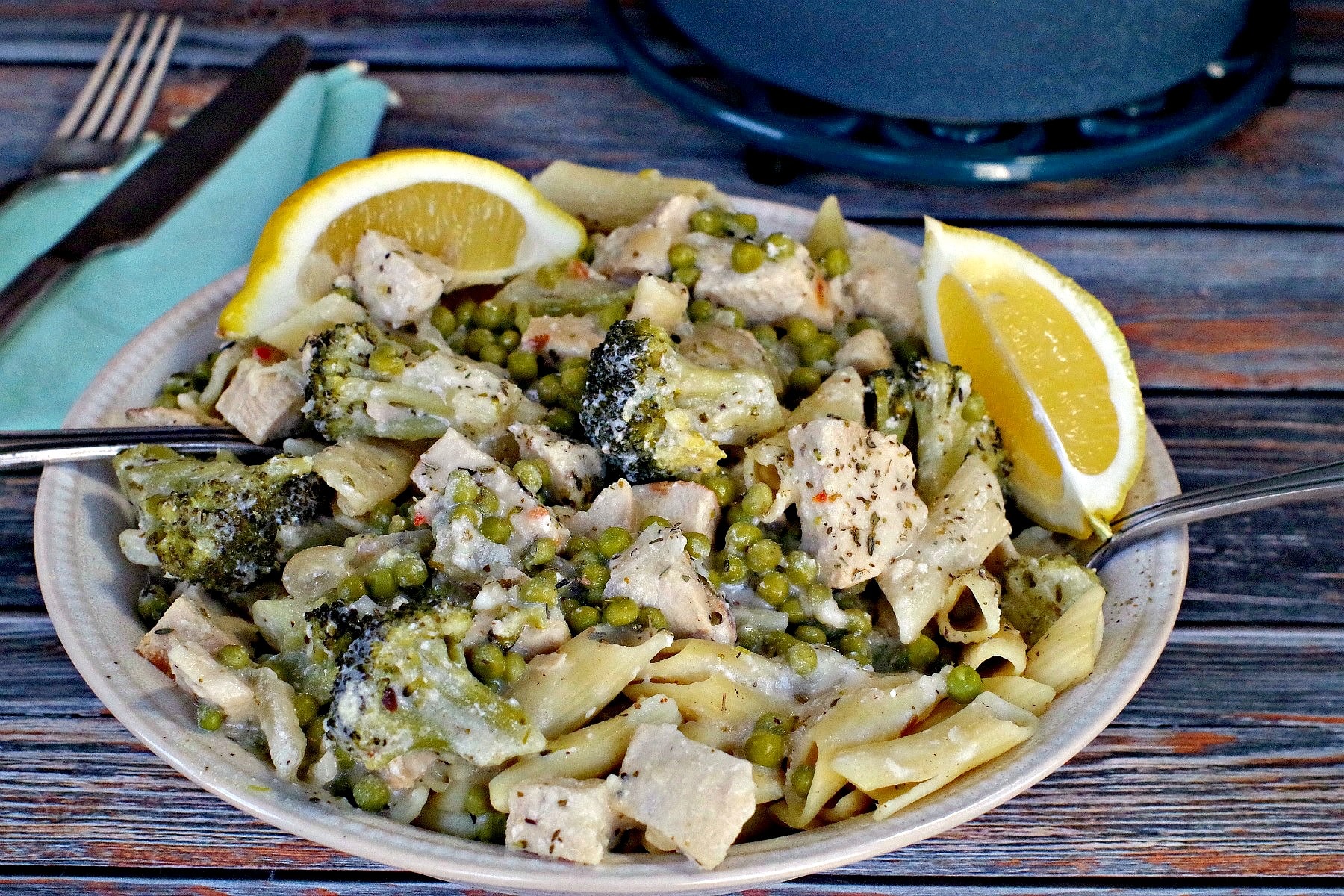 Creamy Lemon Chicken Pasta in a bowl with lemon wedges and blue ceramic pot in background