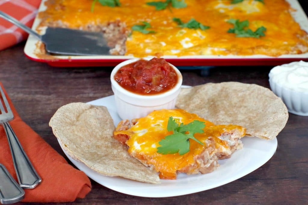 Huevos Rancheros on a white plate with tortillas and salsa and sheet pan (with more) in background