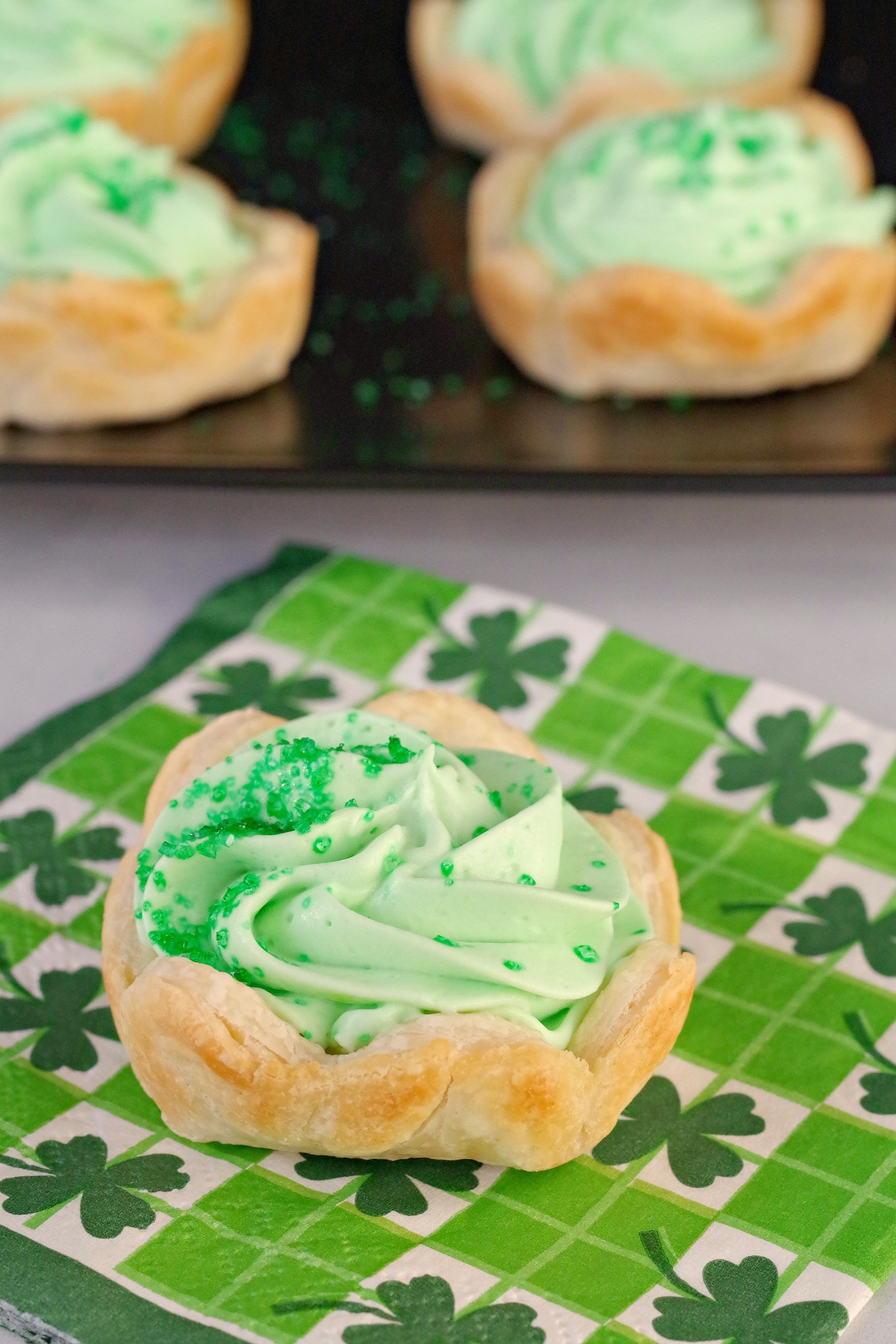 shamrock tart on shamrock napkin with tray of tarts in the background