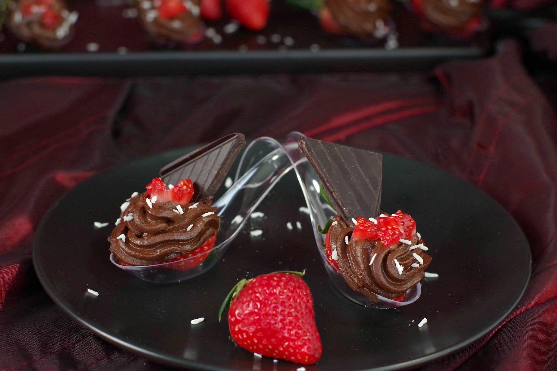 2 Healthy Valentine's Day Desserts on spoons crossed over each other with a whole strawberry in the middle