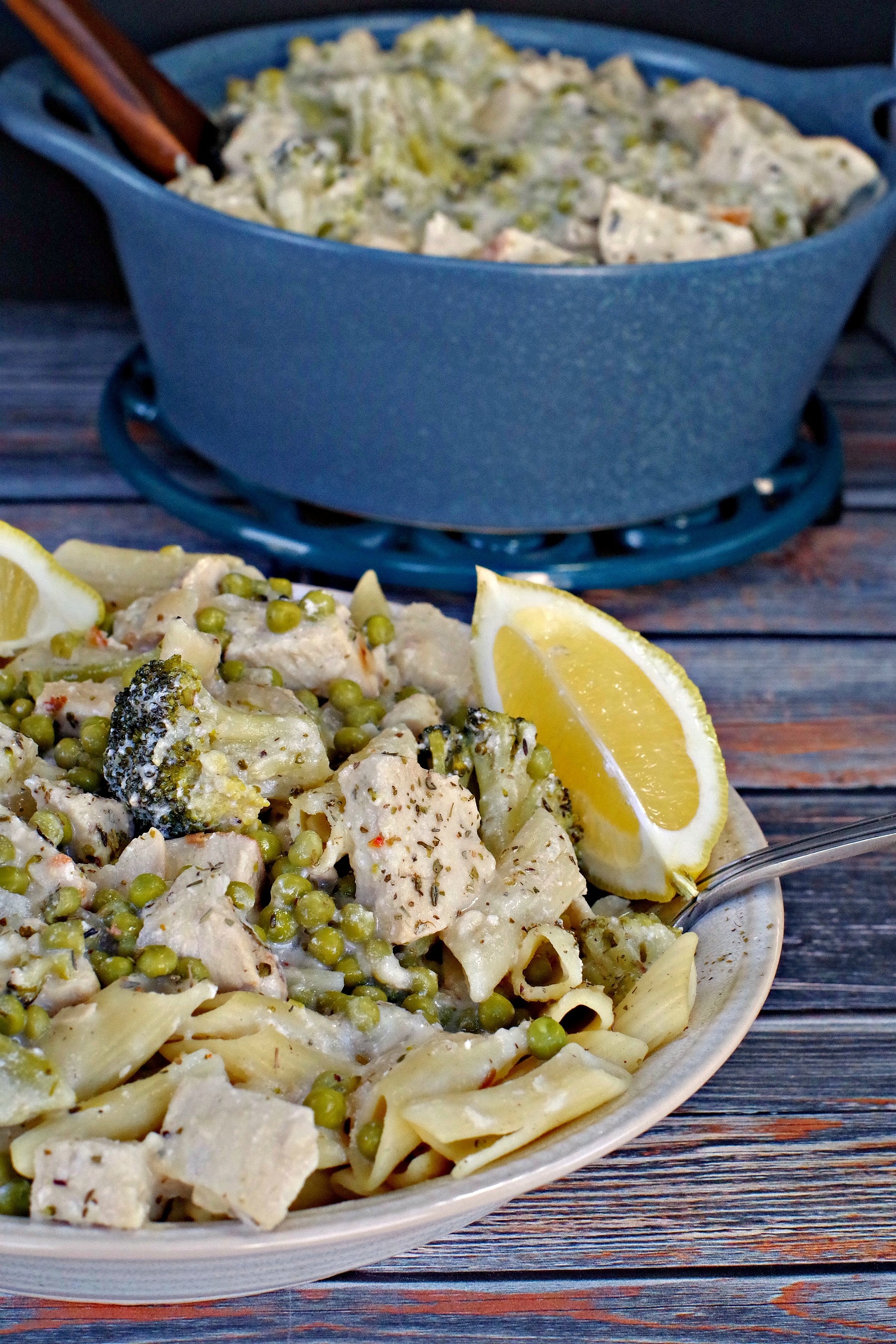 Creamy Lemon Chicken Pasta in a bowl with lemon wedges and blue ceramic pot in background