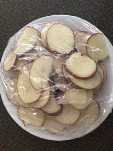 sliced potato on white plate covered in saran wrap