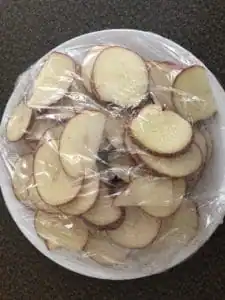 sliced potato on white plate covered in saran wrap