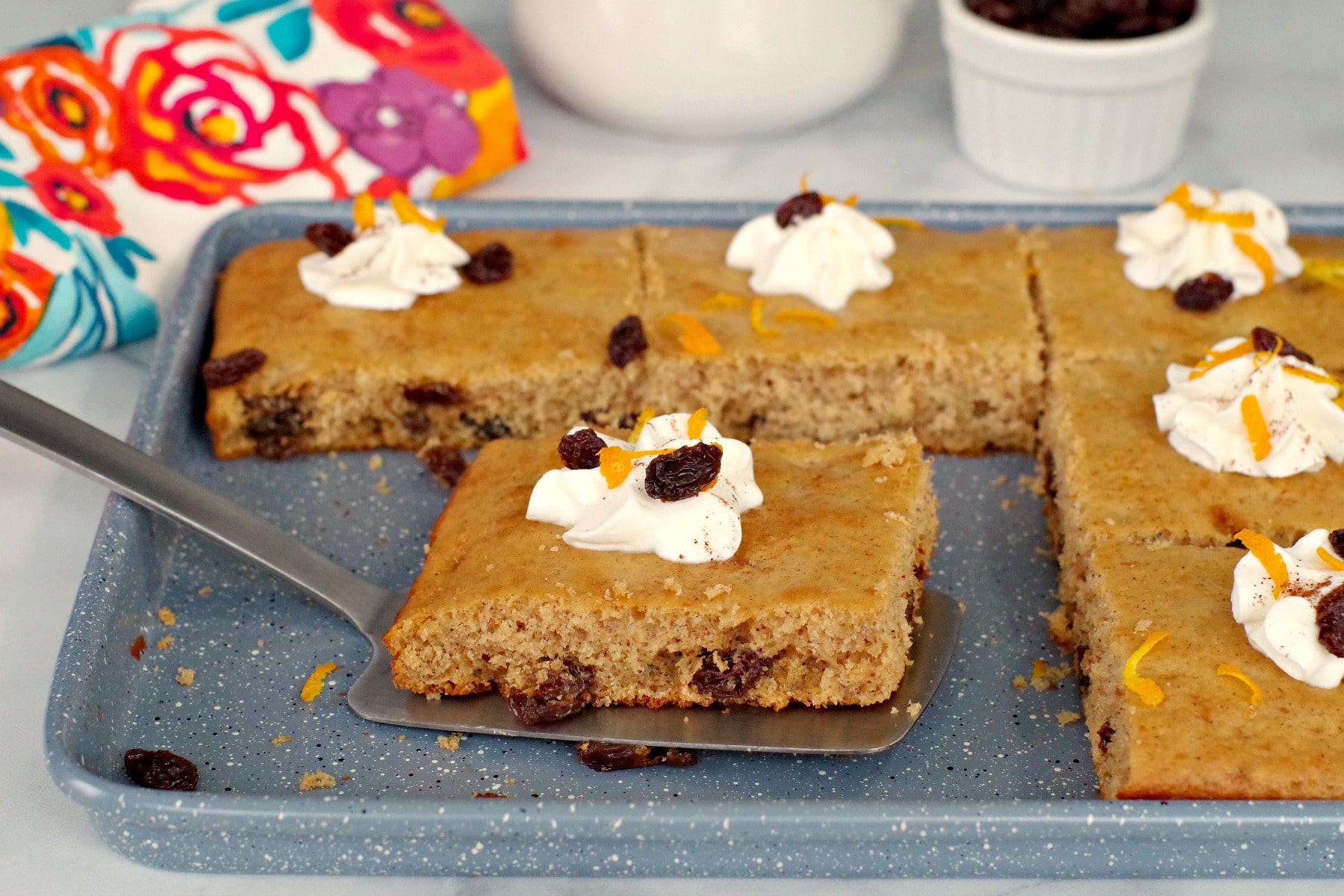 Rum & Raisin sheet pan pancake piece on a spatula being lifted off of blue baking sheet