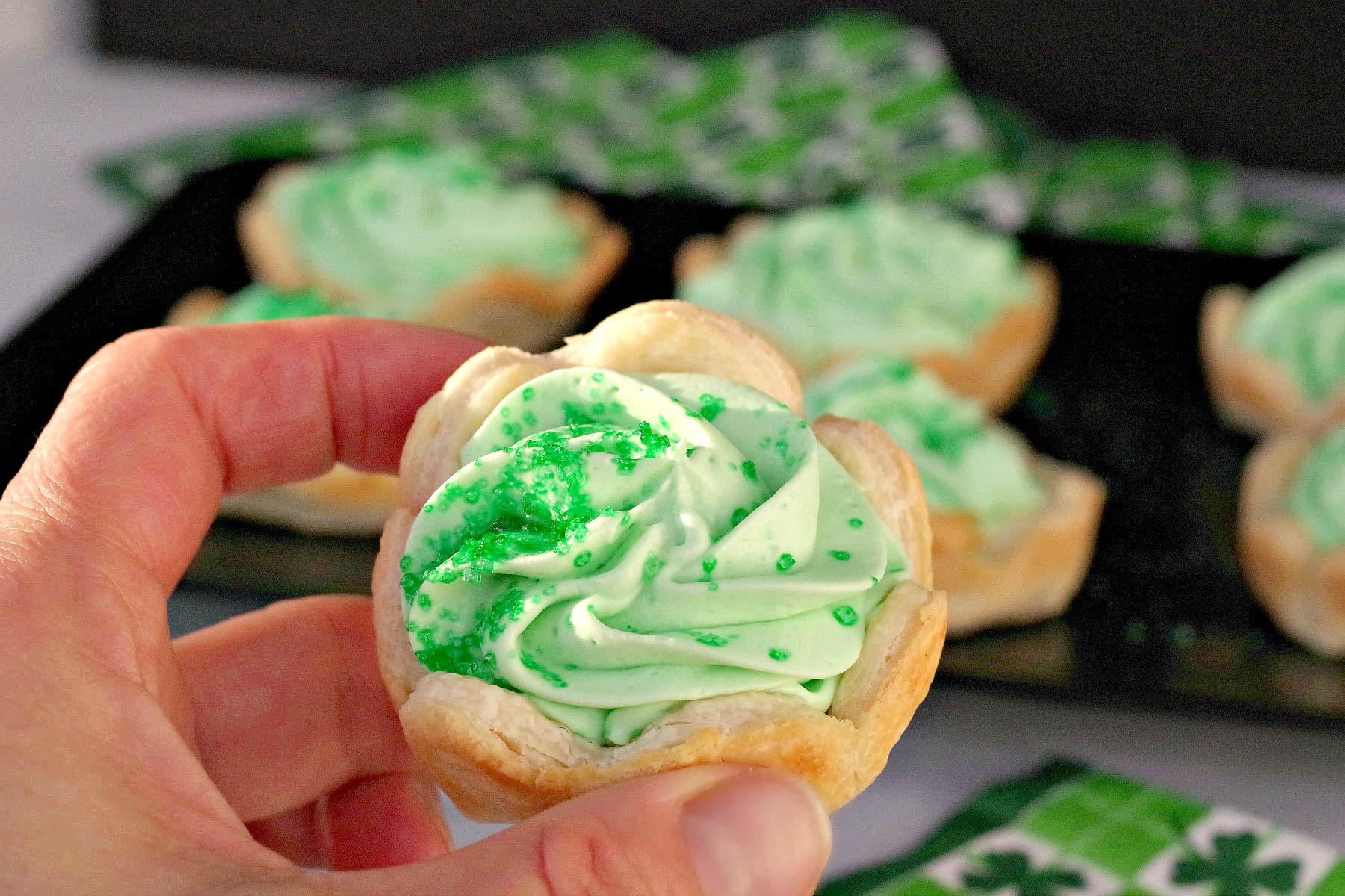 shamrock tart being held with black tray of tarts in the background