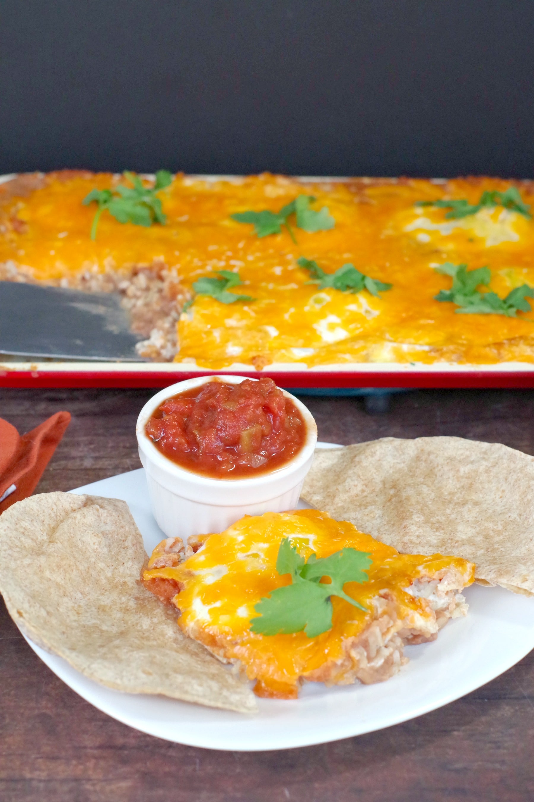 Huevos Rancheros on a white plate with tortillas and salsa and sheet pan (with more) in background