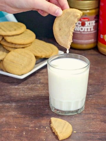 cookie butter cookie being dipped into a glass of milk