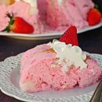 Piece of strawberry jello angel food cake on white plate with whole cake in background