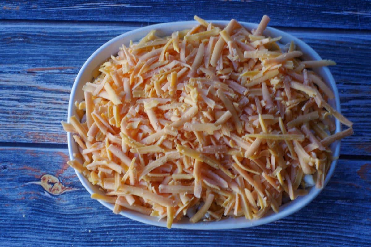 tuna casserole covered with grated cheddar cheese in a white casserole dish