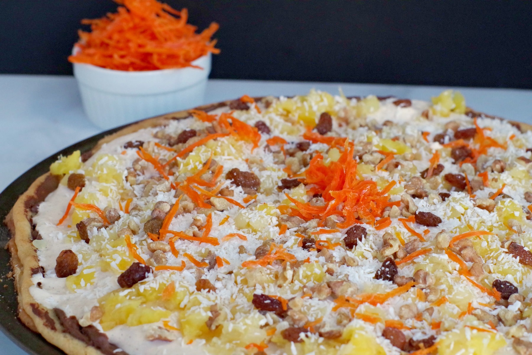 bowl of candied carrots behind carrot cake dessert pizza