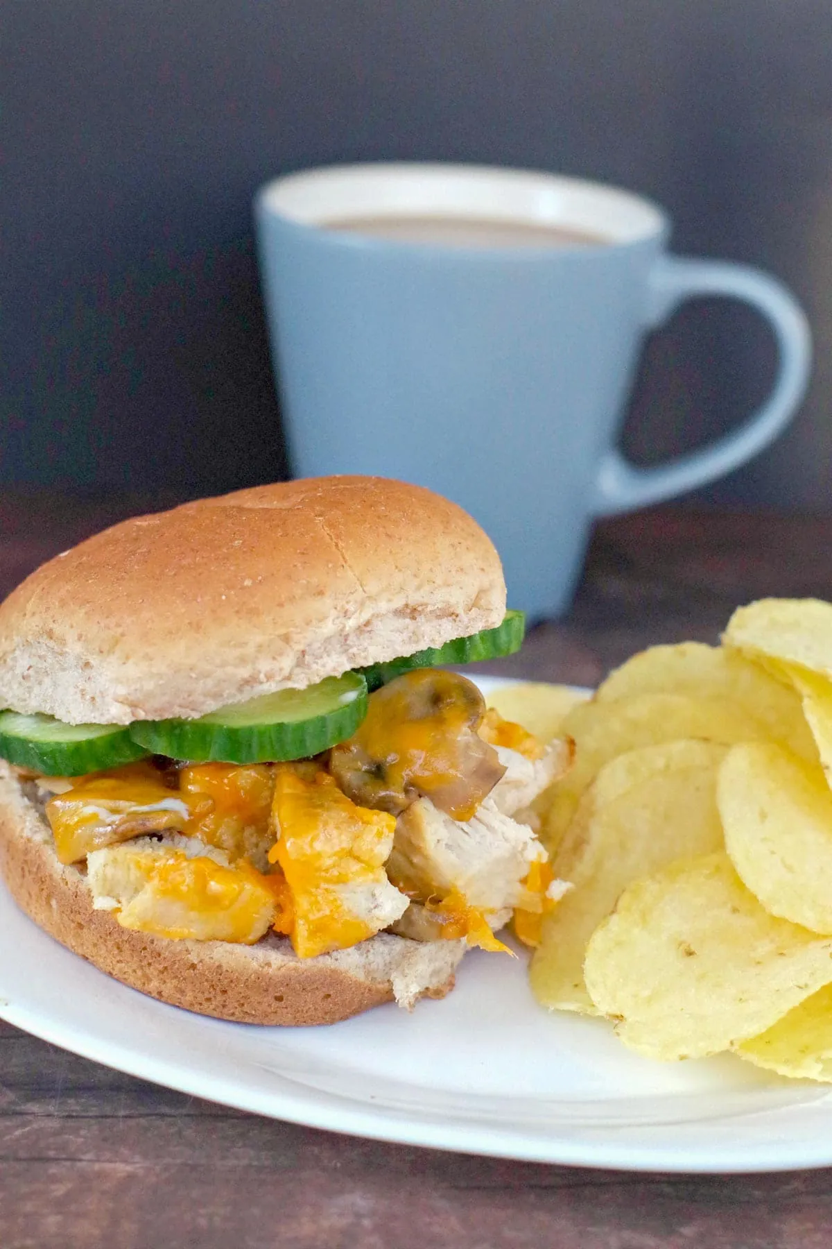 chicken breast burger on a white plate with potato chip and blue coffee mug in the background