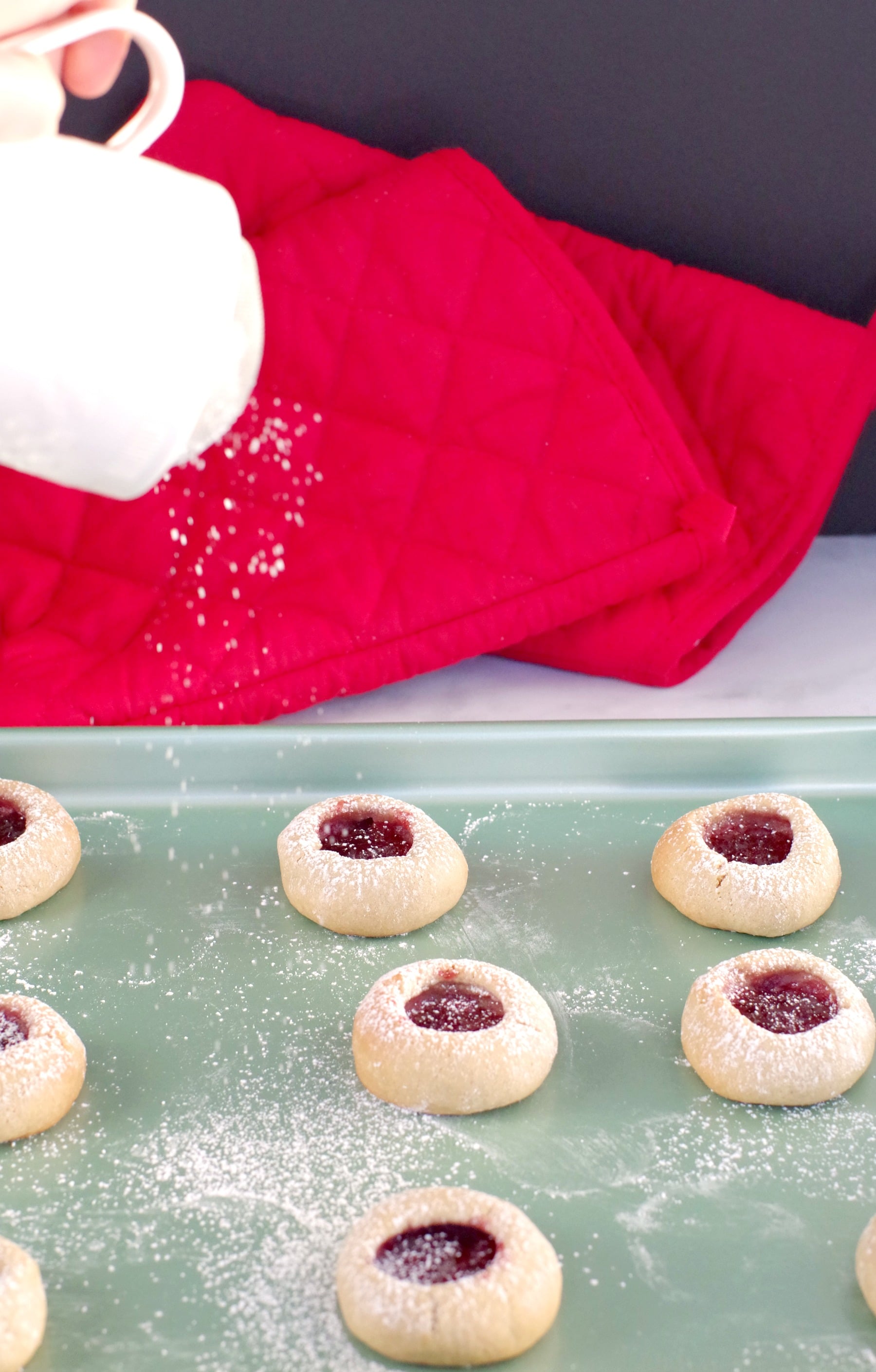 jam cookies on a green cookie sheet with powdered sugar being sprinkled on top