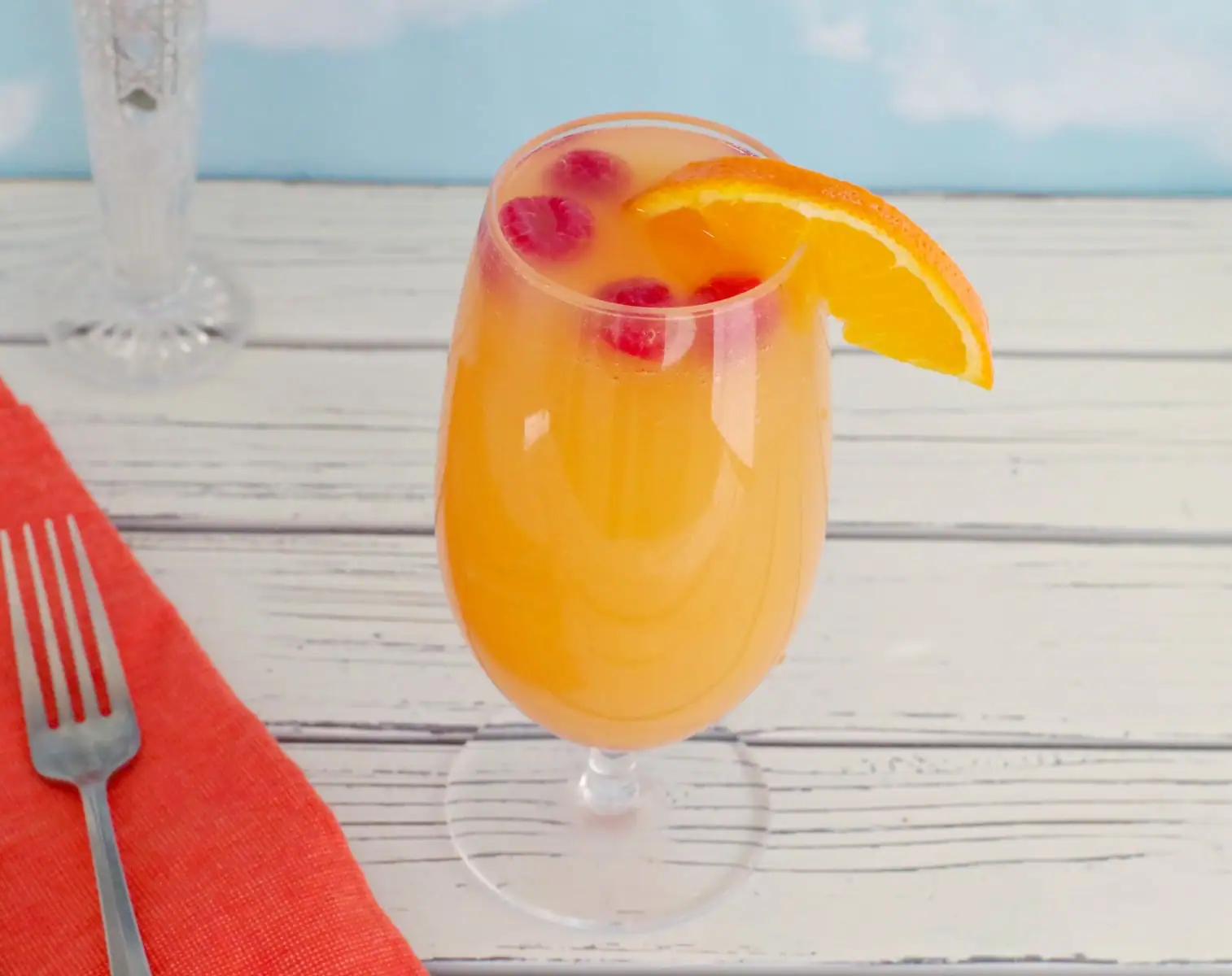 mimosa drink with raspberries and orange garnish