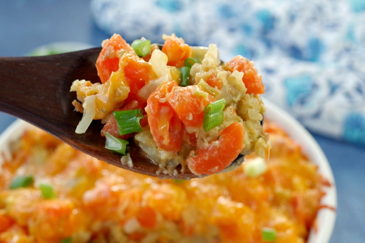 carrot casserole being held up on a dark wooden spoon over a casserole dish full of carrot casserole