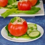 tuna stuffed tomato on a white plate with cucumbers on the side