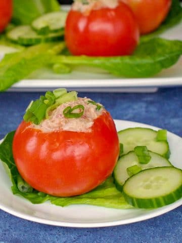 tuna stuffed tomato on a white plate with cucumbers on the side