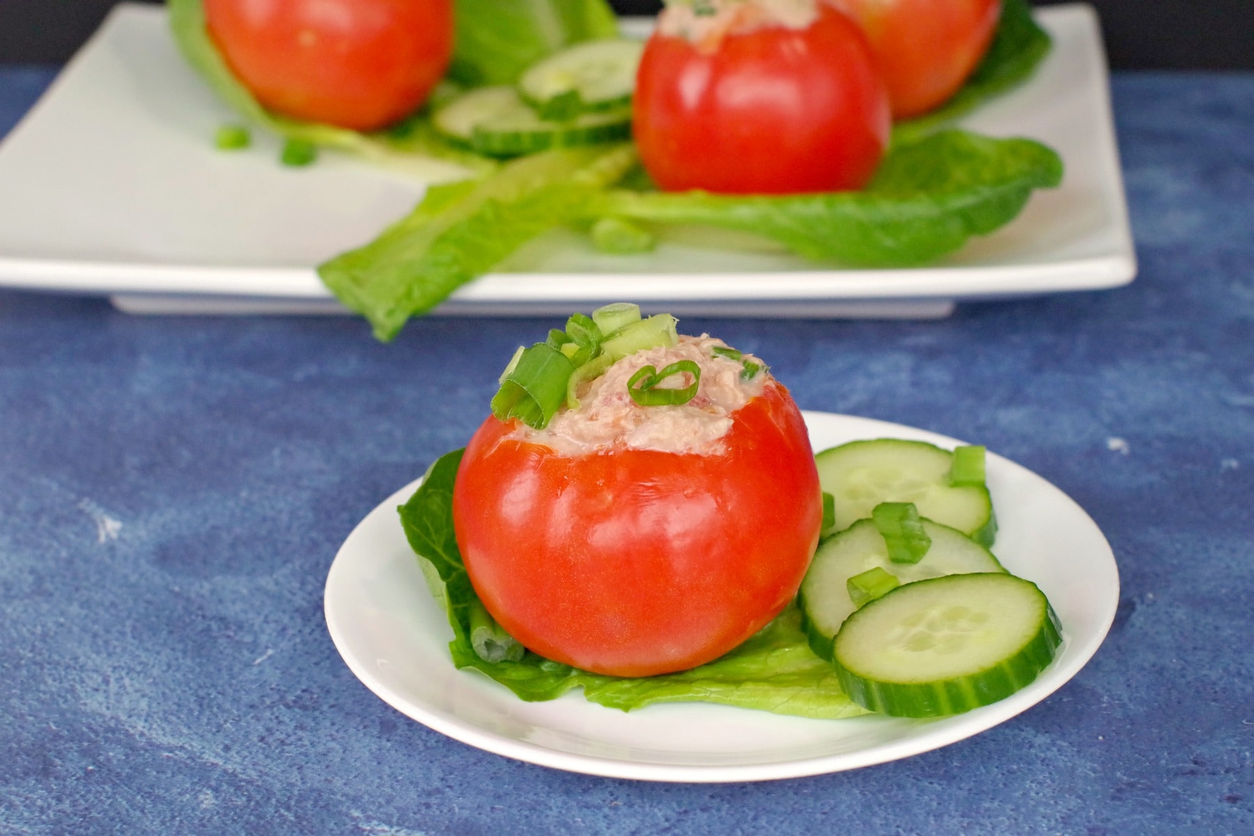 Tuna stuffed tomato on white plate with 3 more tomatoes on platter in background