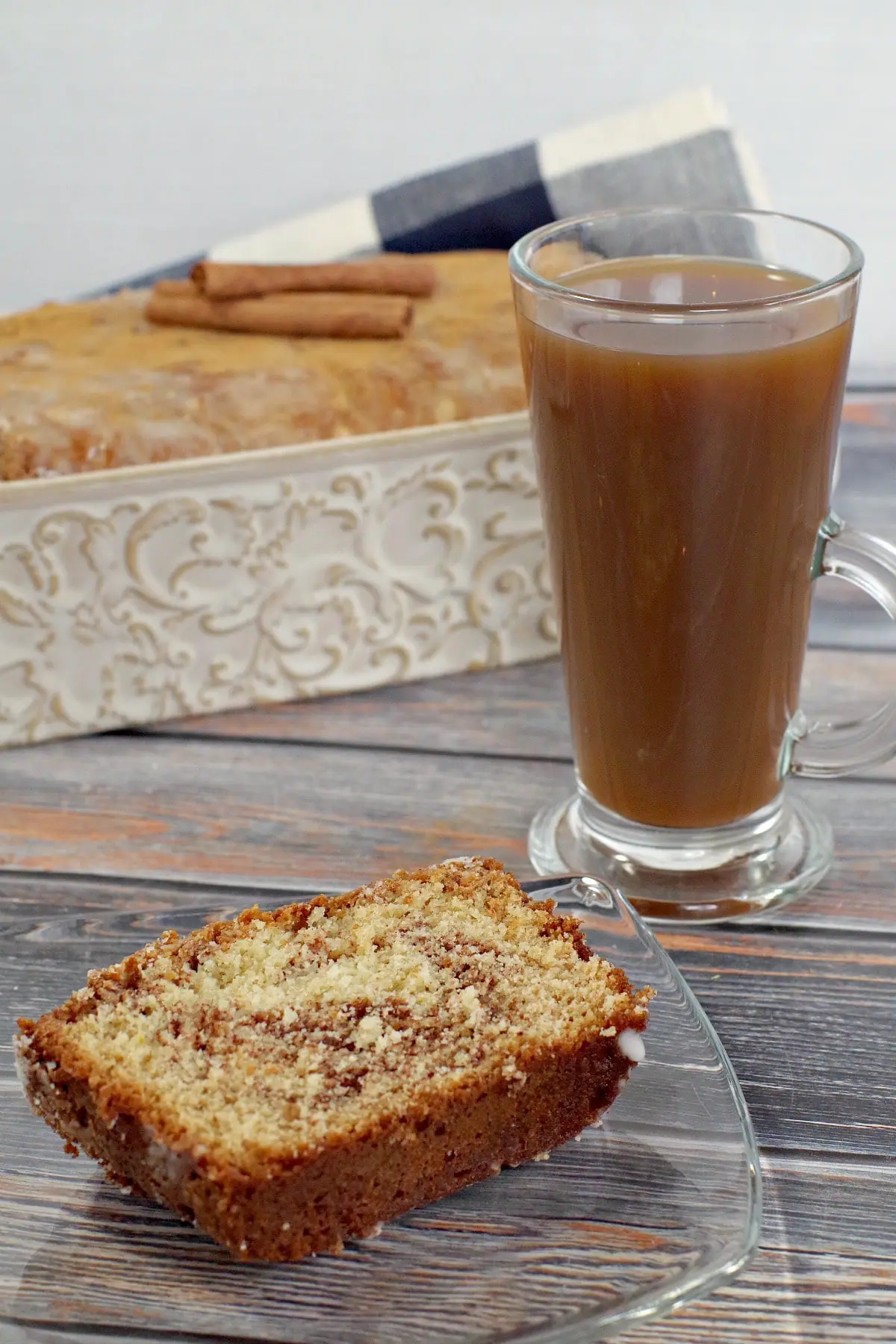 slice of cinnamon bread on a glass plate next to a cup of coffee and loaf pan in background