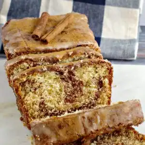 cinnamon loaf on marble cutting board with blue and white checkered tea towel in background