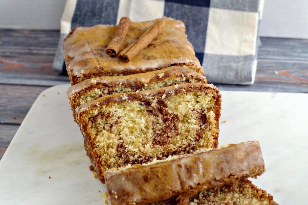 cinnamon loaf on marble cutting board with blue and white checkered tea towel in background