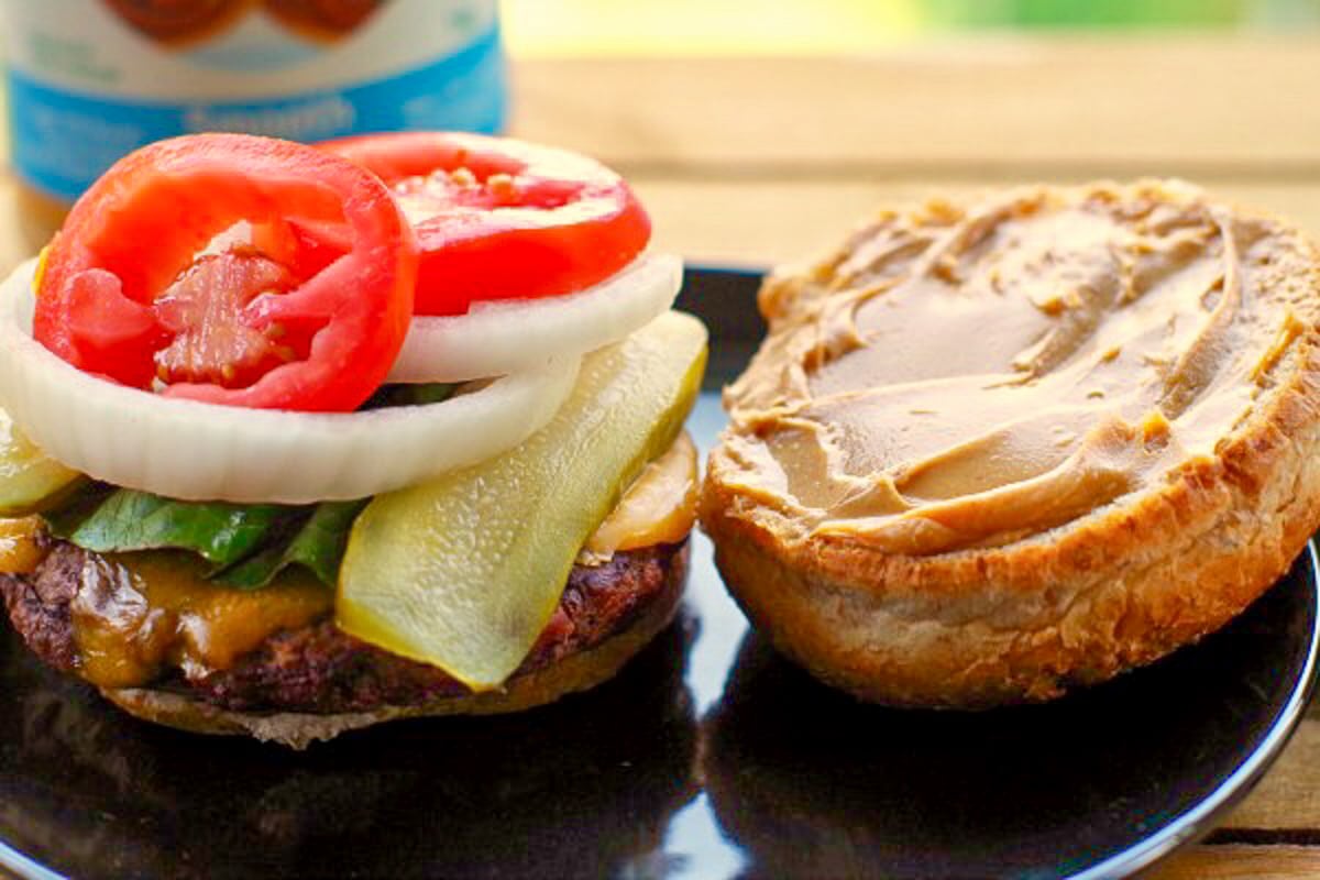 open Peanut butter burger on a black plate with burger and toppings on one side of the bun and peanut butter on the other