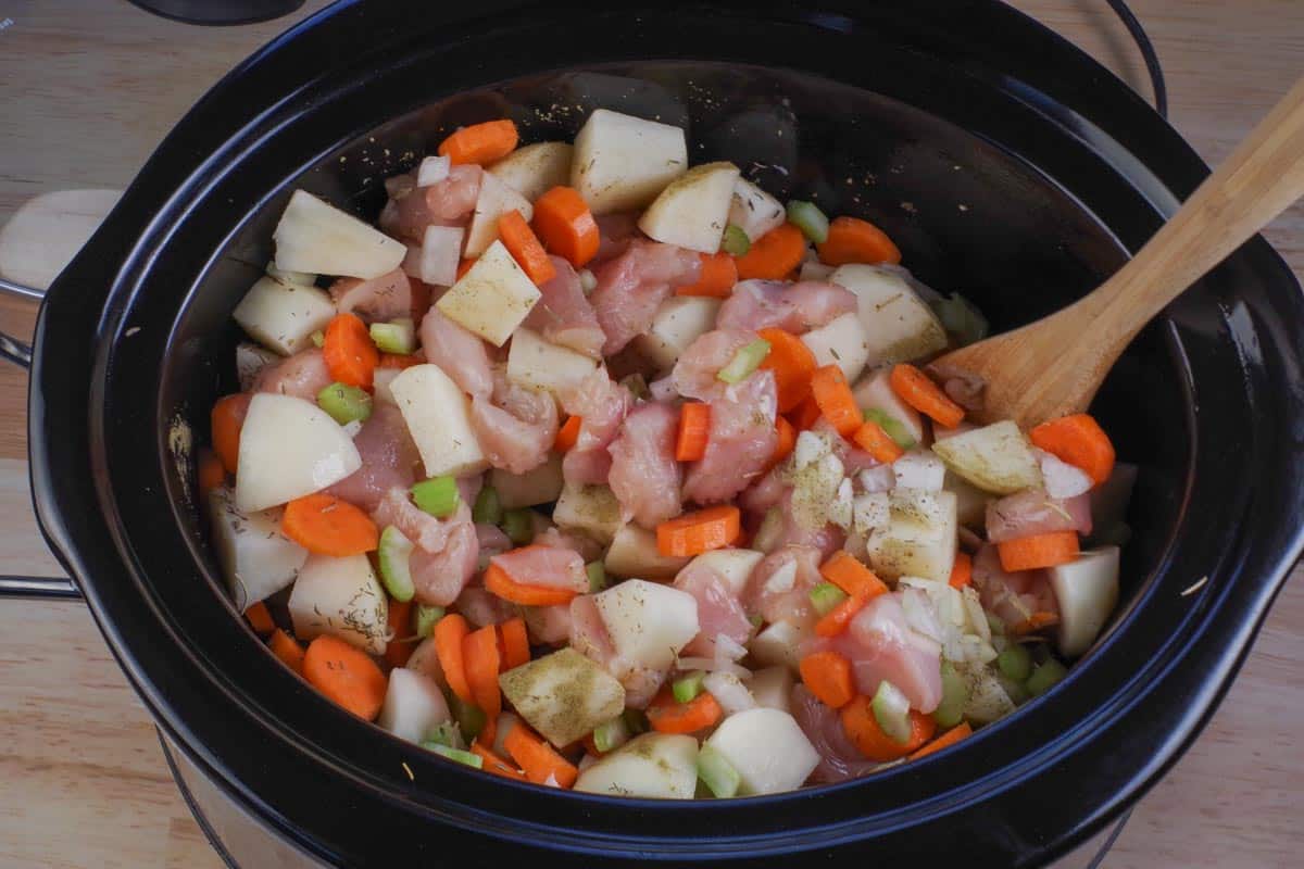 ingredients in healthy slow cooker chicken stew stirred together in crock pot