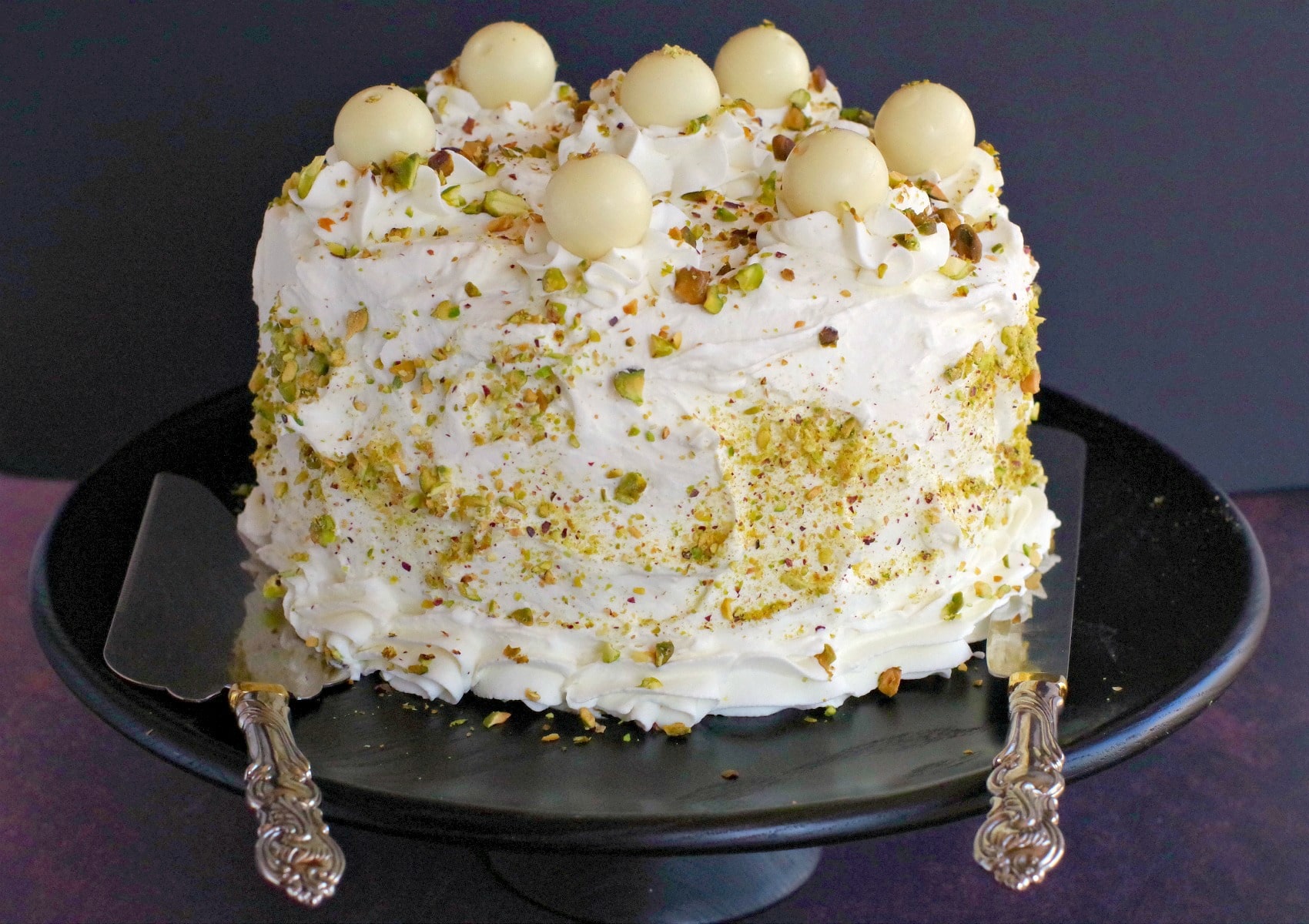 Pistachio Cake on black stand with cake lifter and knife resting on each side