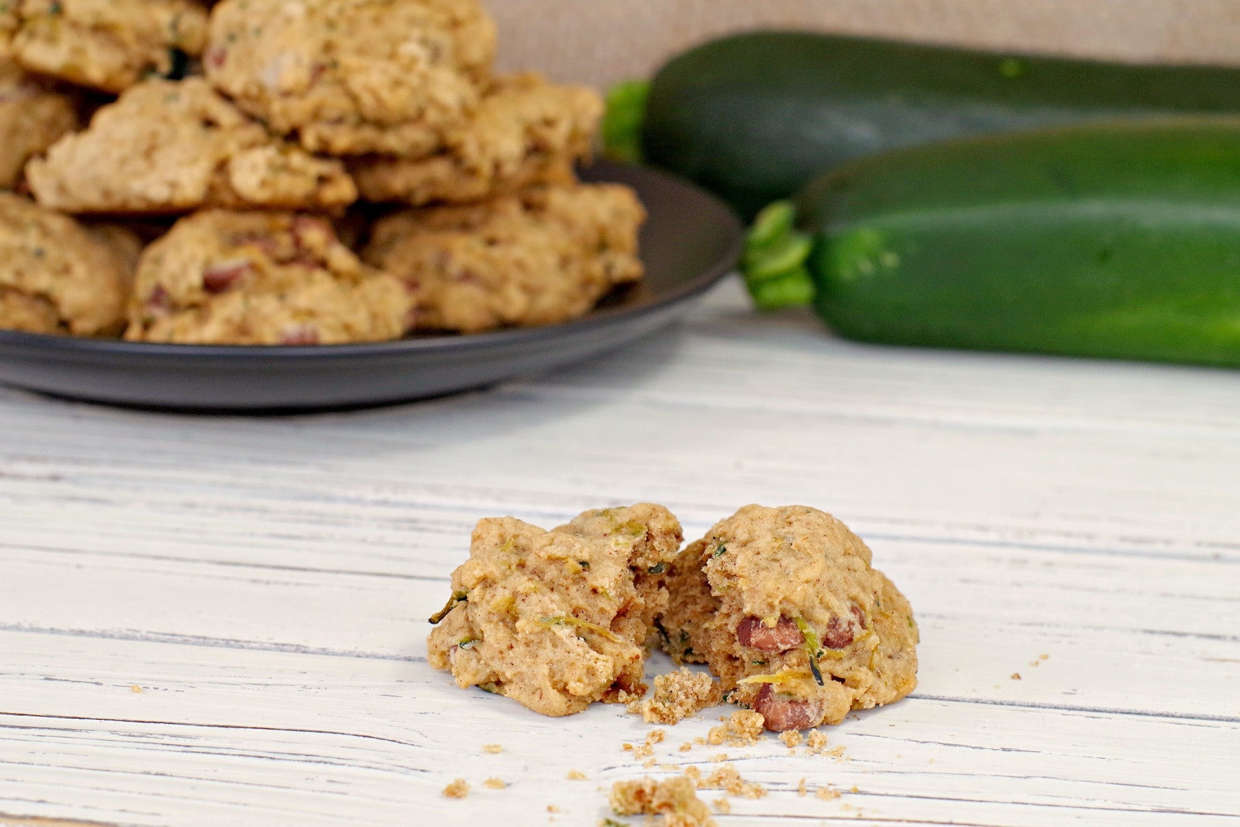 Plate of zucchini chocolate chip cookies in background with one broken apart cookie in front