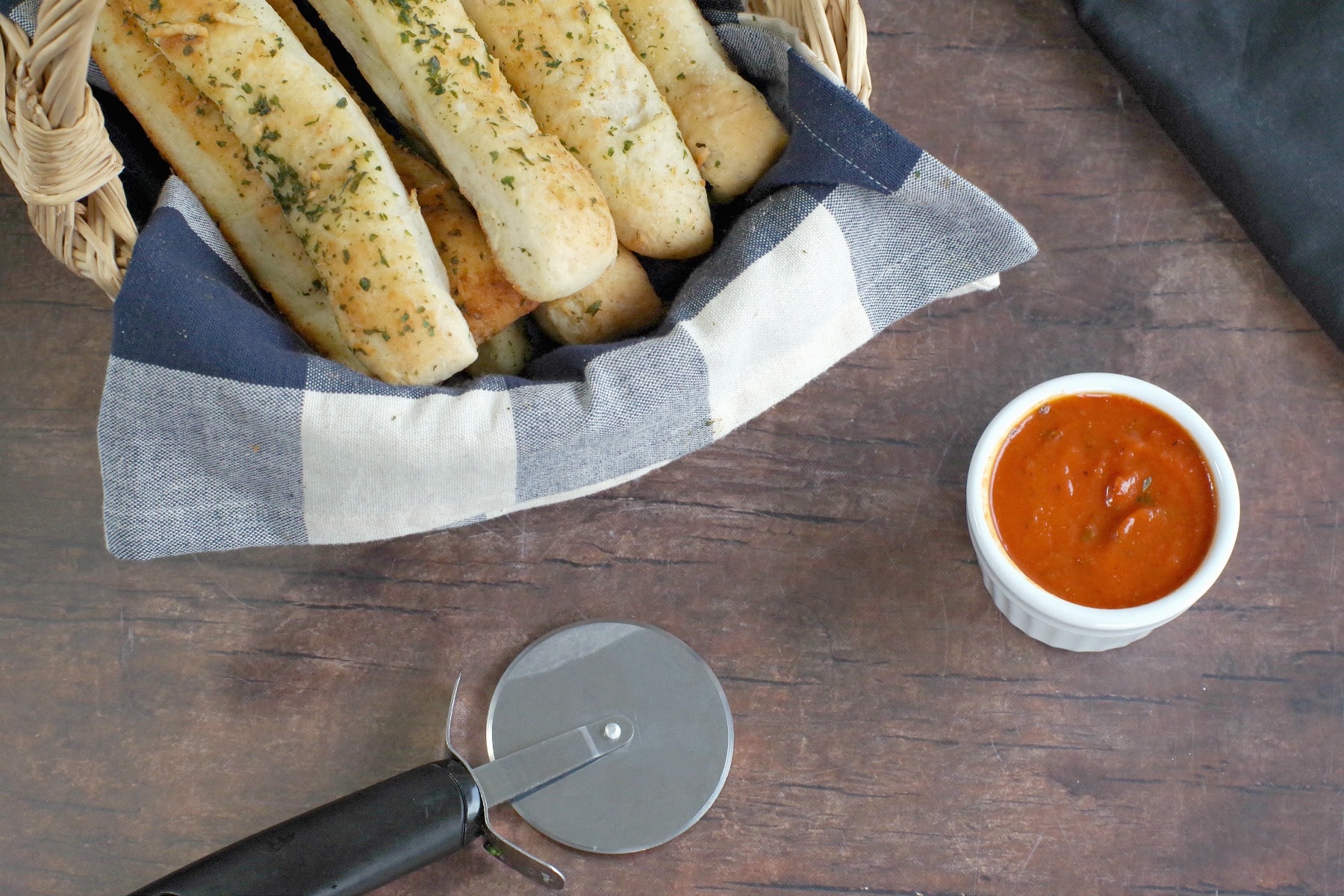 Italian breadsticks in a basket with pizza sauce on the side and a pizza cutter