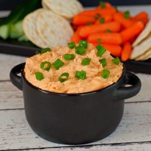 buffalo chicken dip in black container with veggies and crackers in background