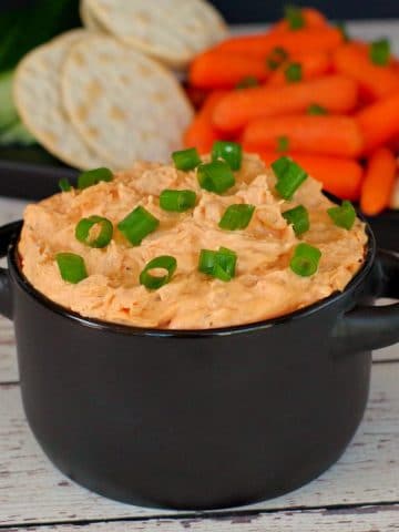 buffalo chicken dip in black container with veggies and crackers in background