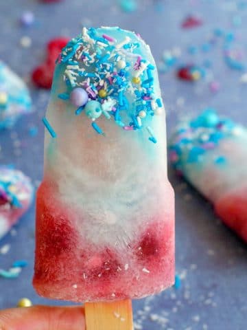 coconut blue raspberry popsicle being held up in front of 3 other popsicles
