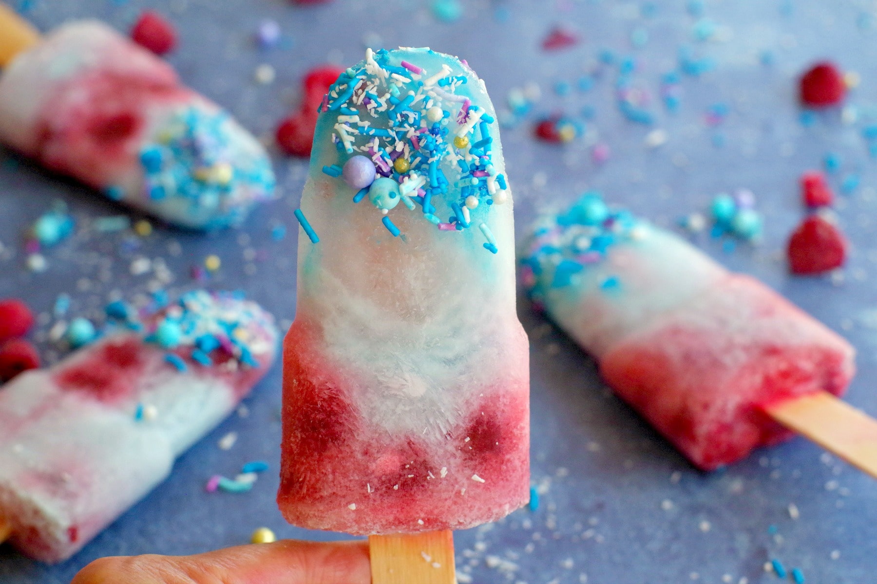 coconut blue raspberry popsicle being held up in front of 3 other popsicles