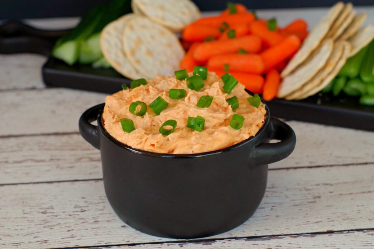 buffalo chicken dip in black container with veggies and crackers in background