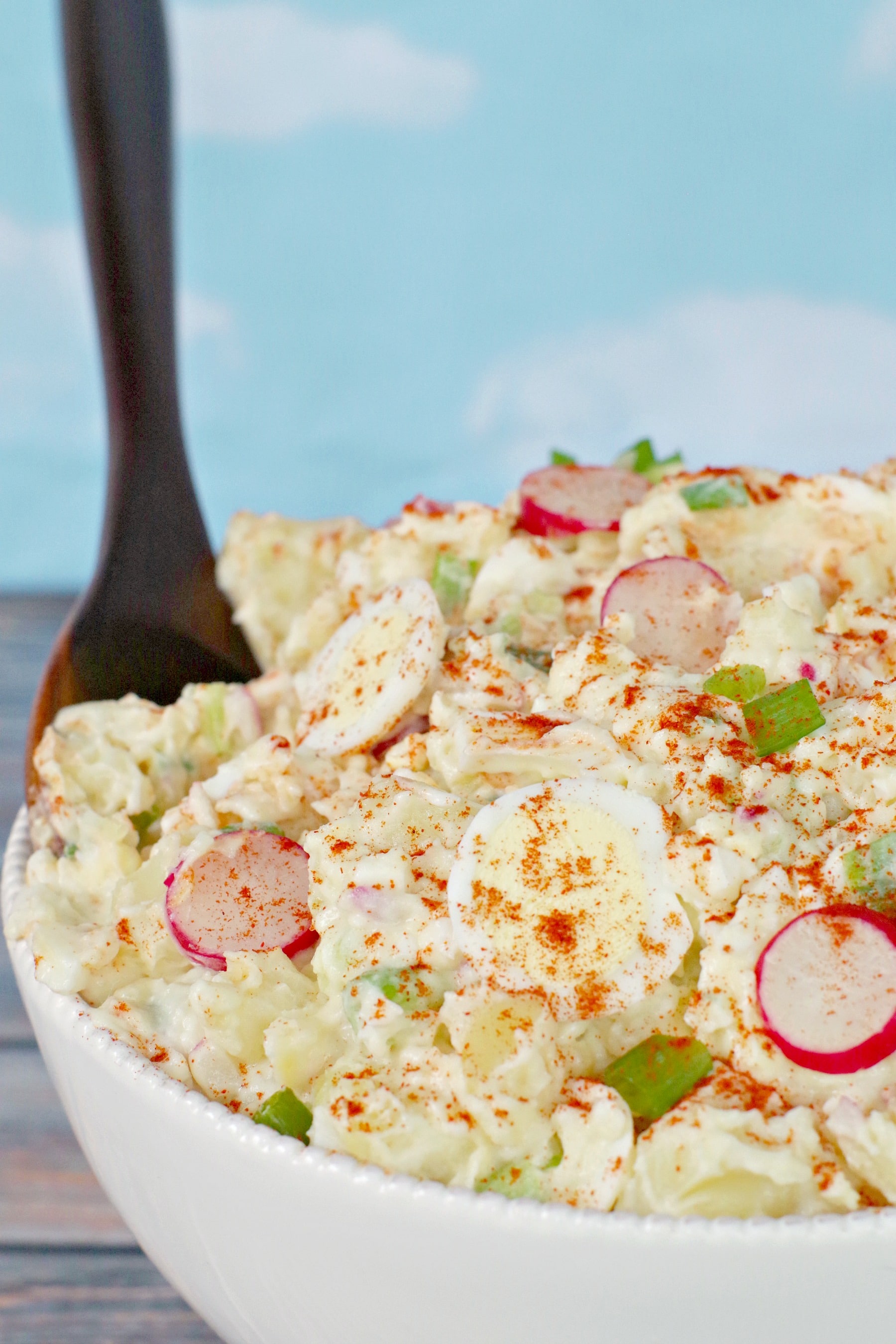 Potato salad in white bowl with brown serving spoon