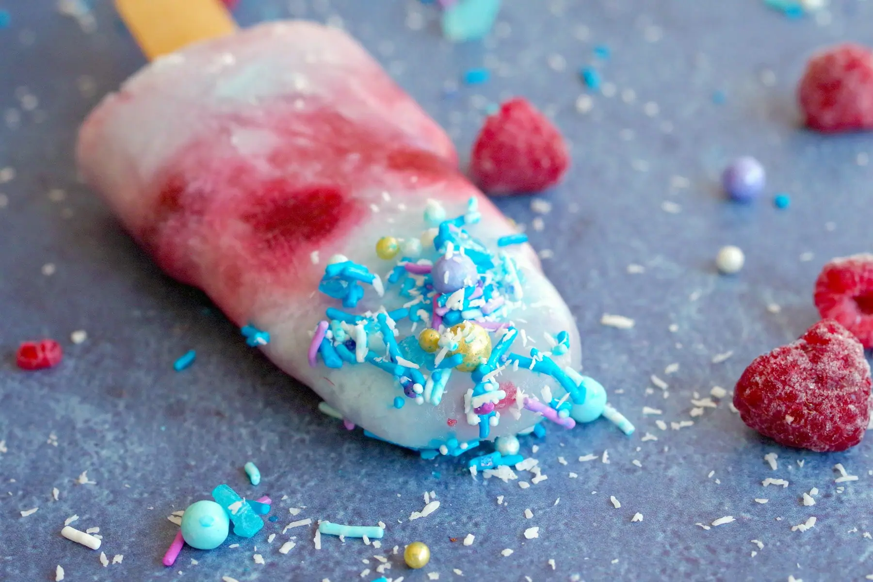 single red white and blue popsicle laying on blue surface with sprinkles