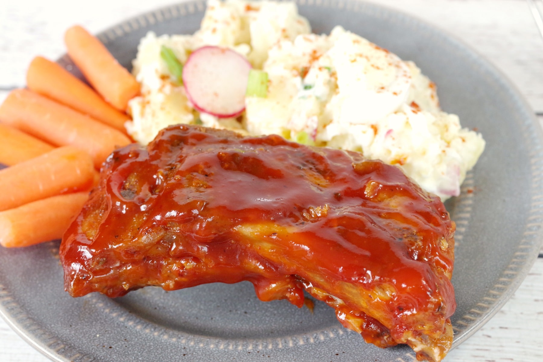 slow cooker BBQ beer ribs on a plate with potato salad and carrots