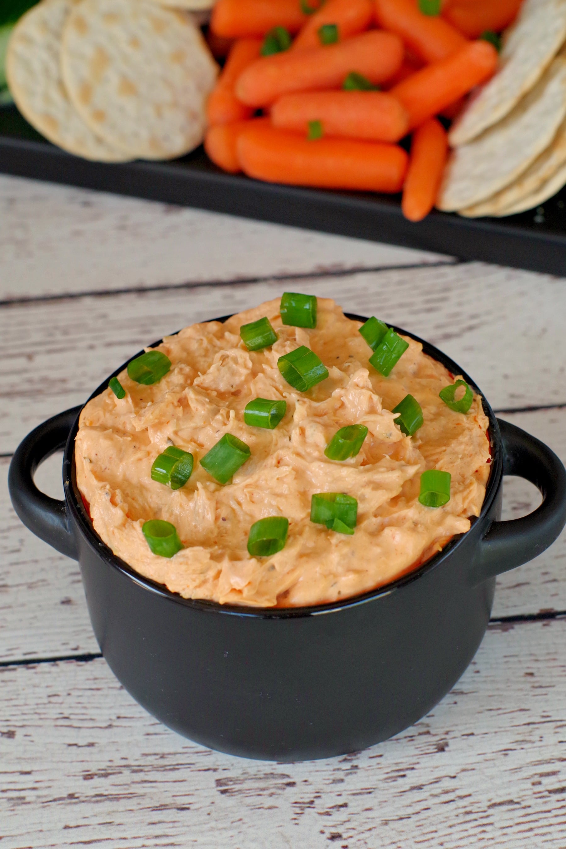 buffalo chicken dip in black container with veggies and crackers in background