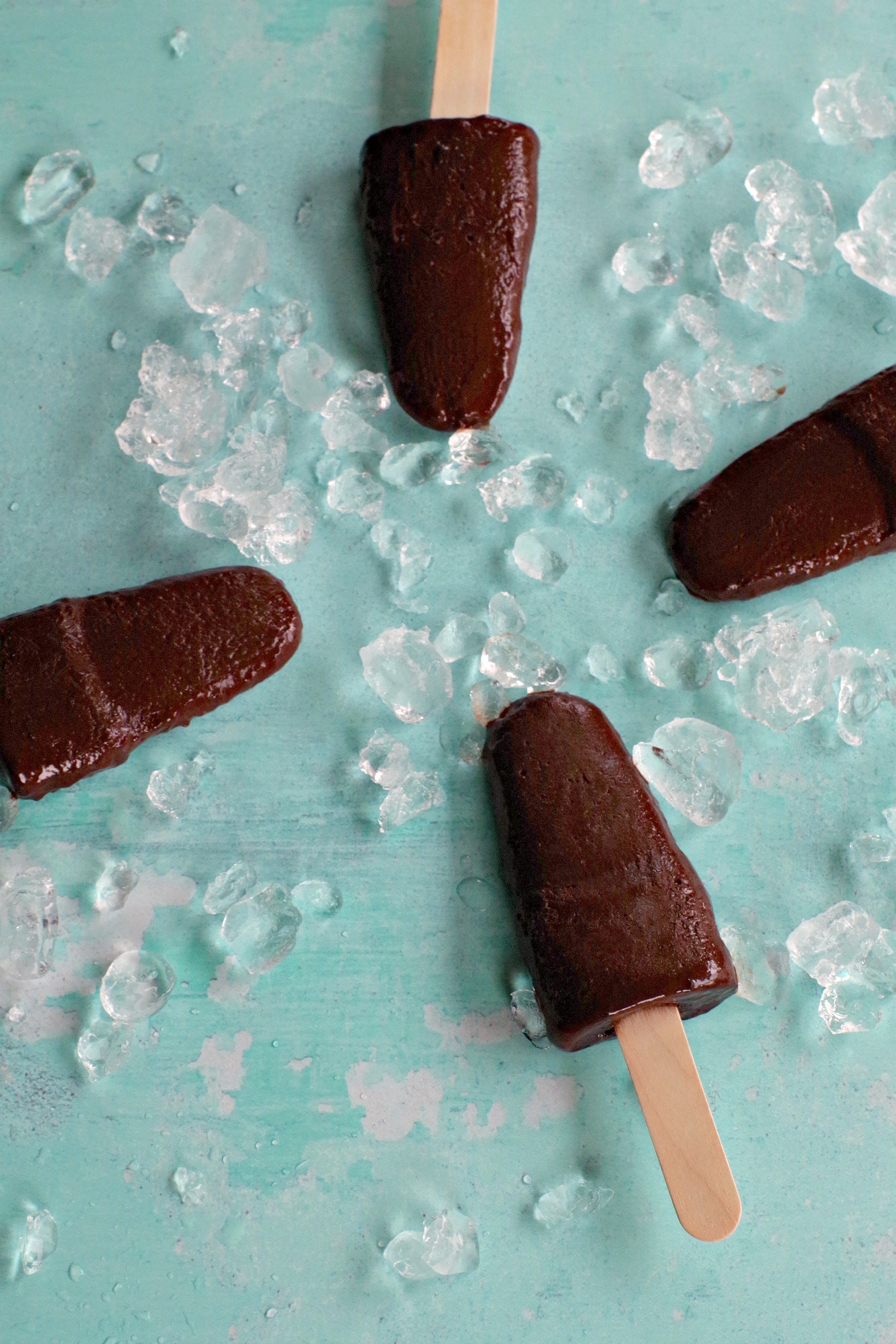 4 chocolate banana popsicles on blue background with ice