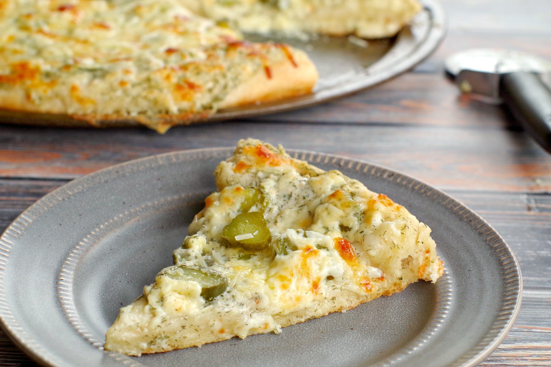 dill pickle pizza on grey plate with whole pizza in background