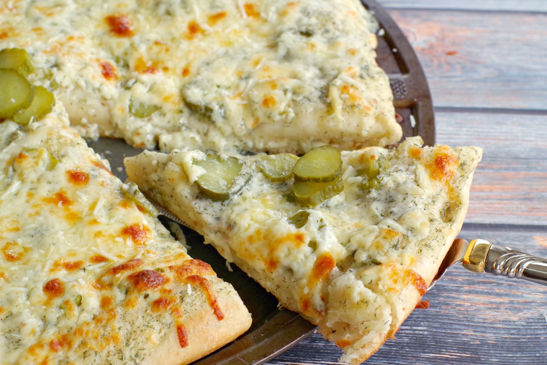 one slice of Pickle Pizza being removed from a whole pizza on a pizza pan