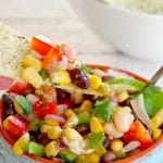 Cowboy Caviar Dip in a bowl with a chip being dipped in