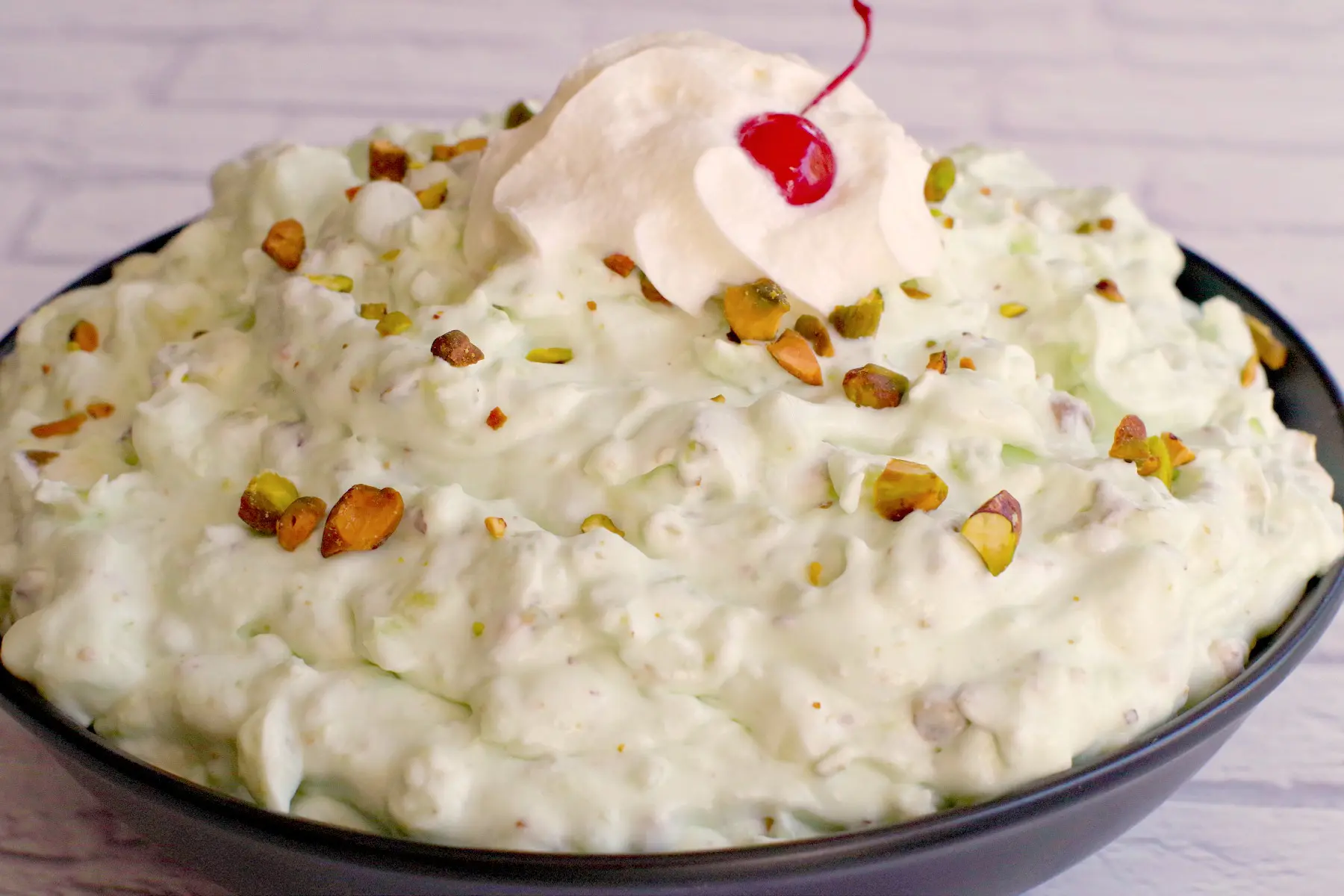 watergate salad in black bowl with whipped cream and cherry
