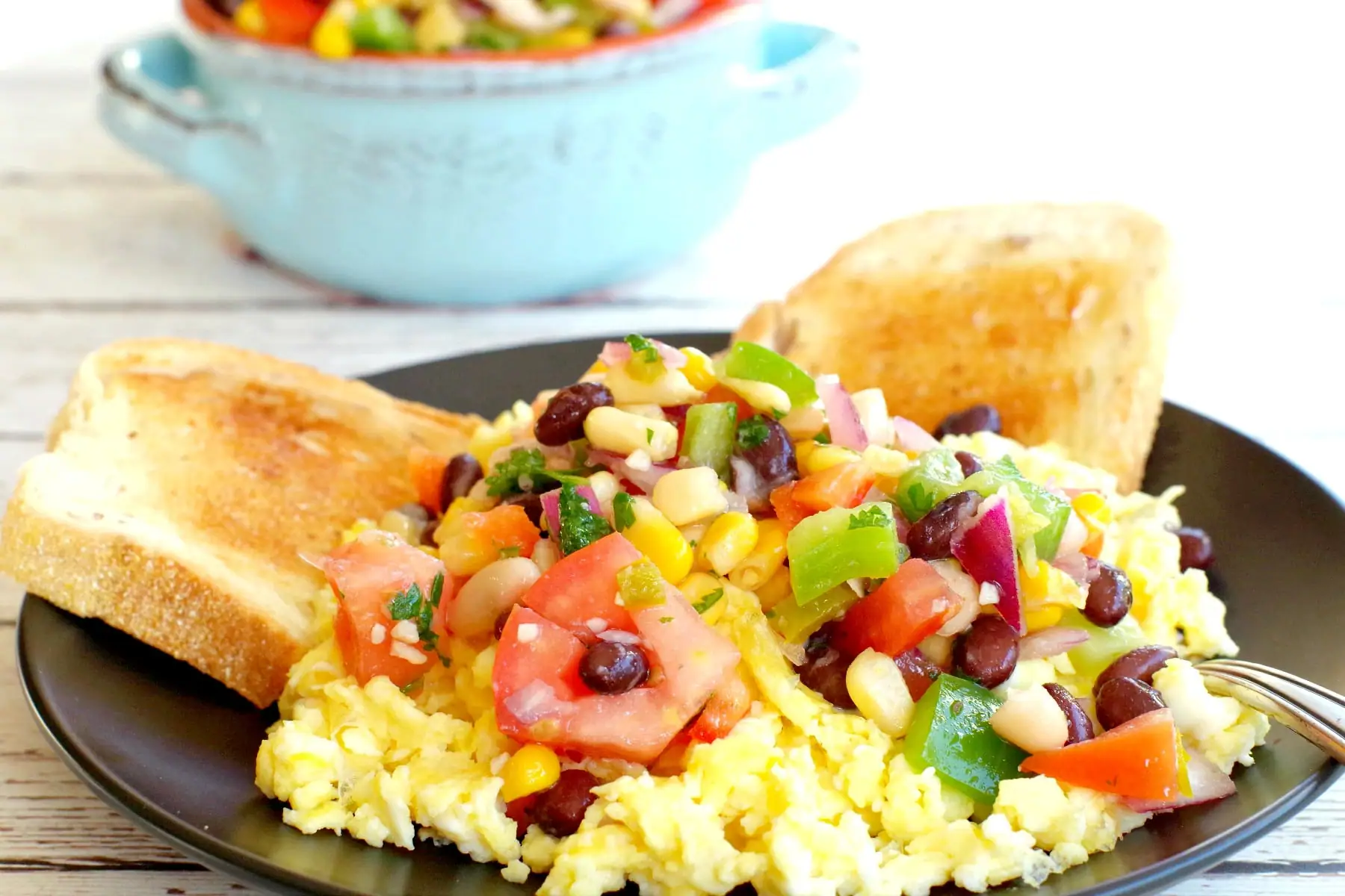 cowboy caviar dip on top of scrambled eggs with toast and dish of dip in the background