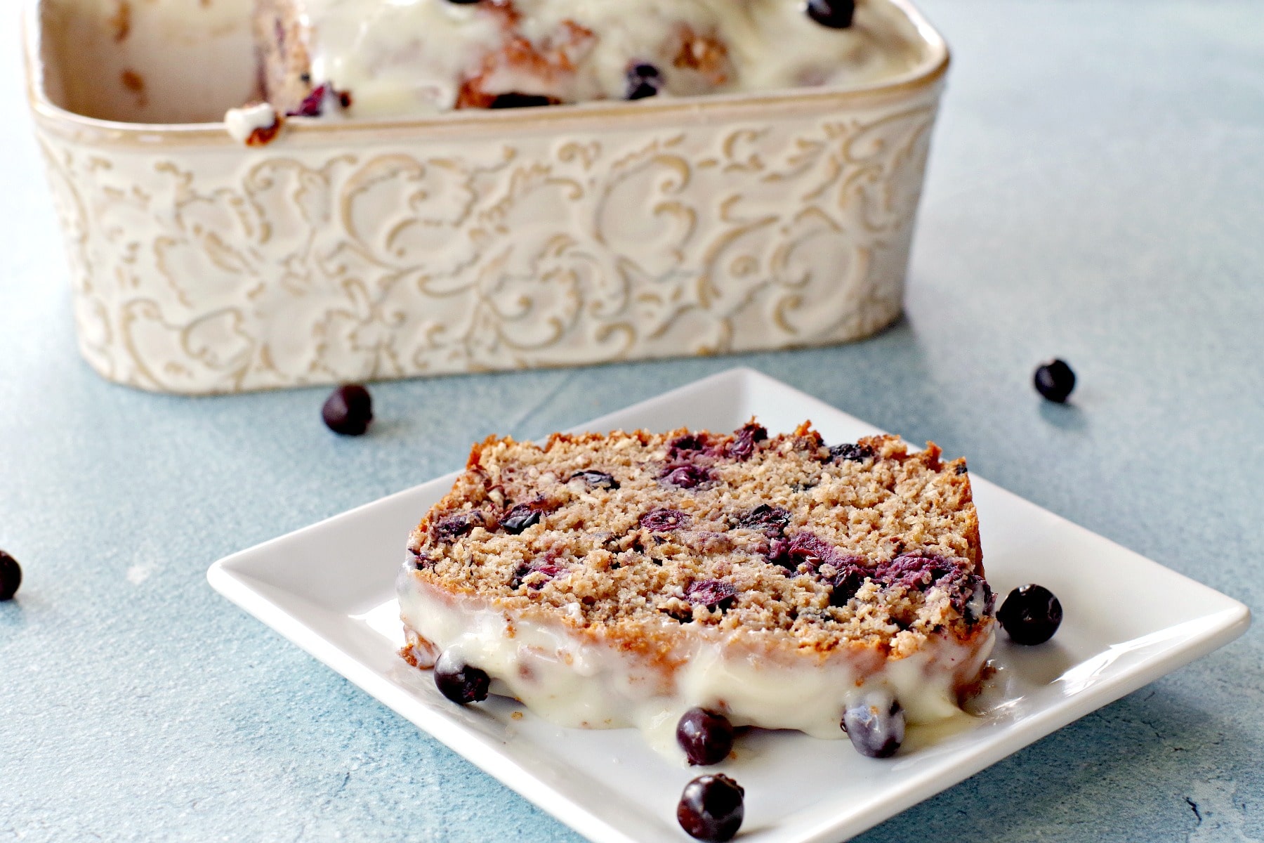 slice of saskatoon berry loaf on white plate with loaf pan in background