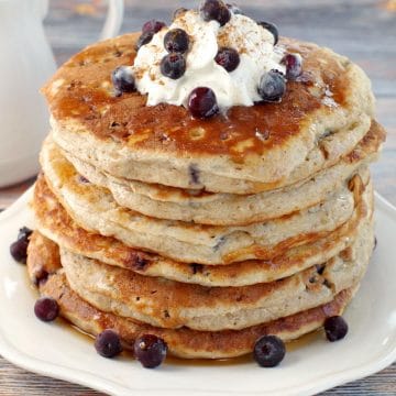 stack of Saskatoon Berry Pancakes with whipped cream and berries on top