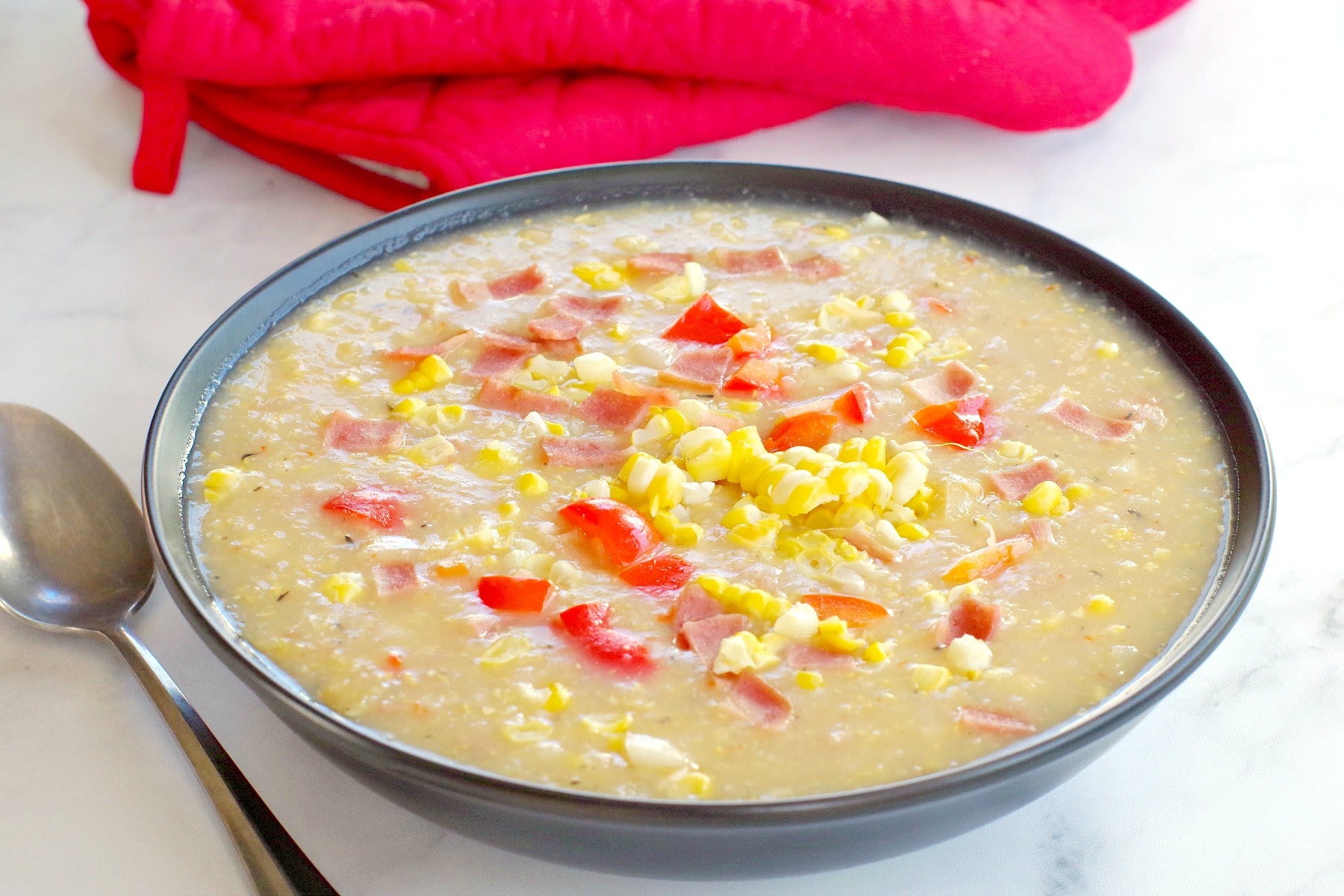 corn chowder in black bowl with red oven mitts in backgroun