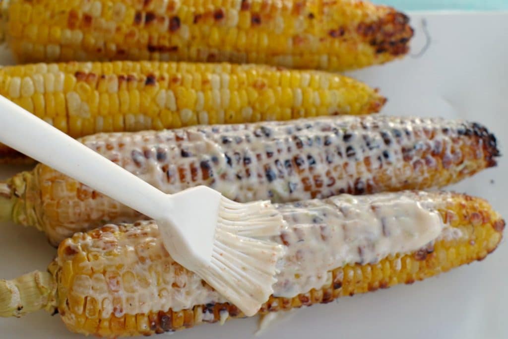 Grilled corn with sauce being spread on it