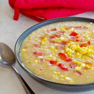 Healthy Corn Chowder in a black bowl, with a spoon on the side and red over mitts in background