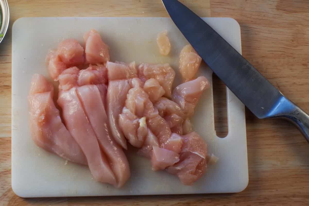 raw chicken breast om white cutting board with sharp knife